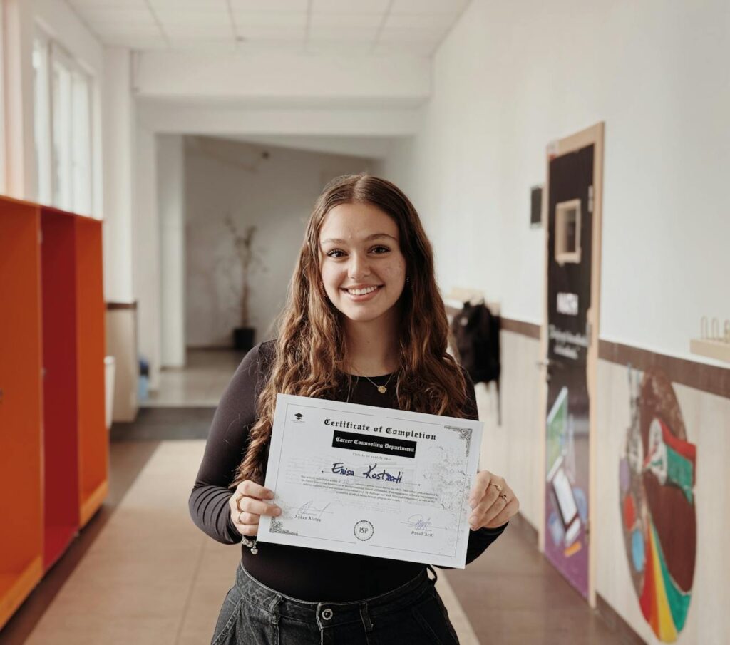 Smiling woman proudly displays certificate in a school corridor. Achievement and success captured.