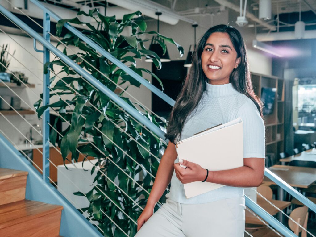 Young female professional smiling and holding documents in a modern office setting.